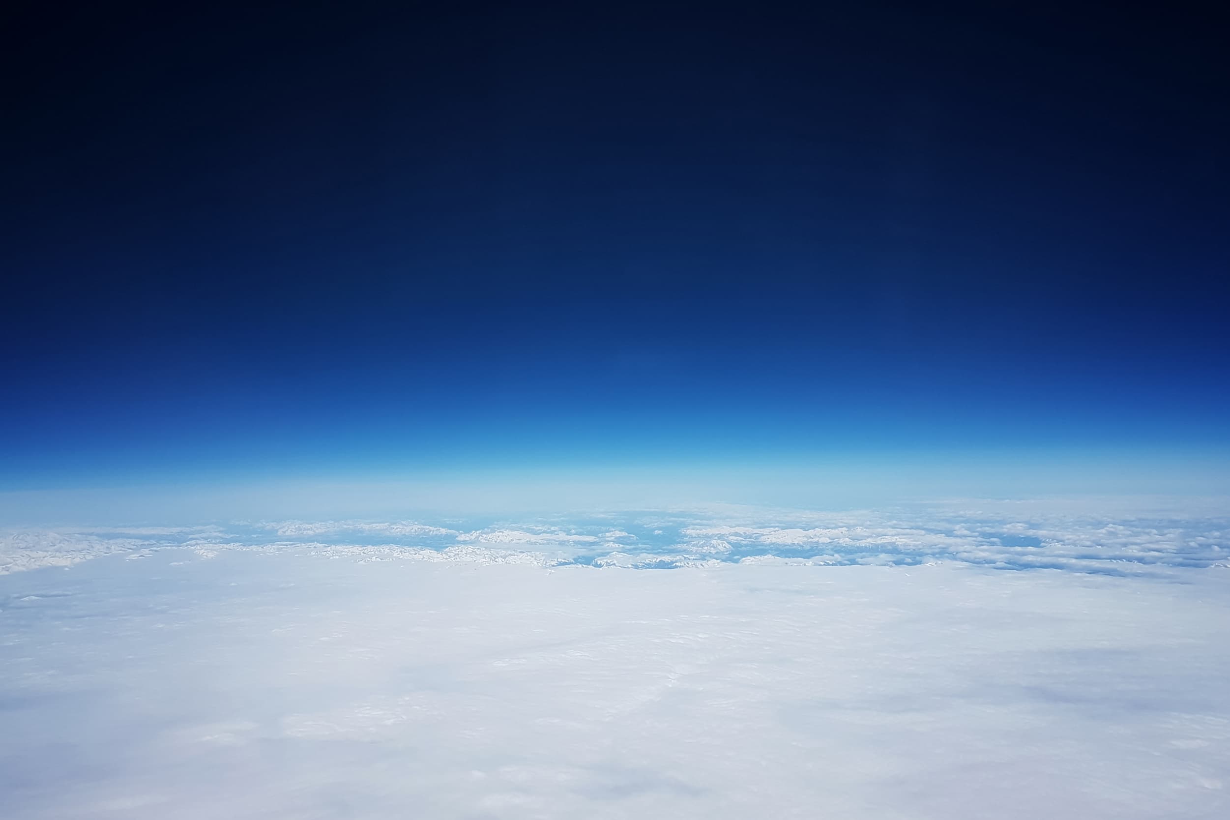 Earth's atmosphere photographed from high altitude, a dense cloud layer beneath a blue sky deepening toward the darkness of space.